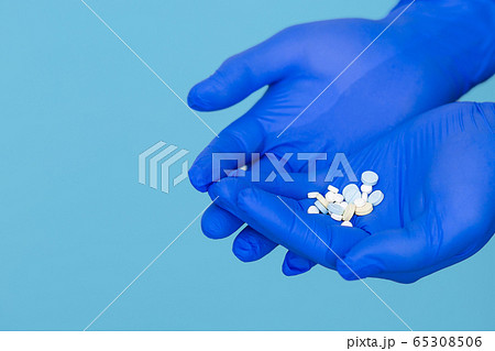 The pills are in the doctor's hands. Hands in blue medical gloves hold pills. Blue isolated background. 65308506