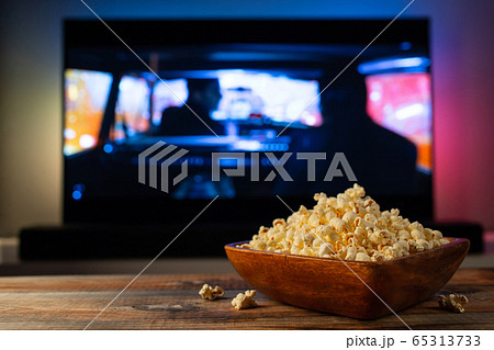 A wooden bowl of popcorn and remote control. 65313733