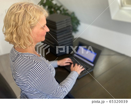A casually dressed caucasian middle aged woman is installing a laptop computer with a stack of several more computers next to her. Laptops are used and second hand, might be for people in need due to A casually dressed caucasian middle aged woman is installing a laptop computer with a stack of several more computers next to her. Laptops are used and second hand, might be for people in need due to 65320039
