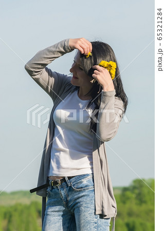 a beautiful girl, a brunette, stands in a flower meadow and adjusts dandelions in her hair a beautiful girl, a brunette, stands in a flower meadow and adjusts dandelions in her hair 65321284