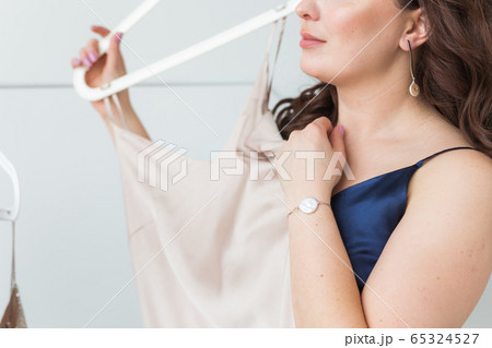 Pretty girl looking at dress while choosing suitable one. Fashion, sale and store concept. 65324527