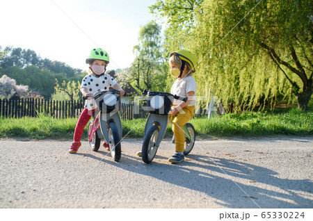 Small children with face masks playing outdoors with bike, coronavirus concept. 65330224