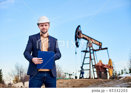 Engineer making notes standing in oilfield, behind him - oil pump jack 65332203