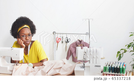 Cute African-American woman using a sewing machine sews clothes Cute African-American woman using a sewing machine sews clothes 65337218