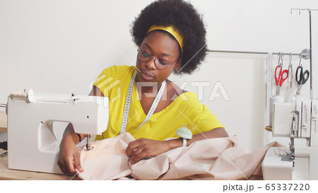 Cute African-American woman using a sewing machine sews clothes Cute African-American woman using a sewing machine sews clothes 65337220