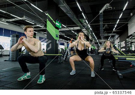 fitness, sport, training, gym and lifestyle concept - group of smiling people exercising in the gym, doing squats fitness, sport, training, gym and lifestyle concept - group of smiling people exercising in the gym, doing squats 65337546