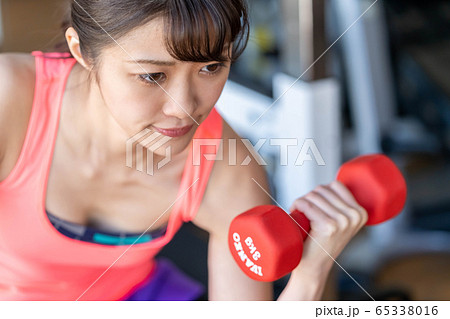 ダンベルで腕の筋肉上腕三頭筋を鍛える真剣な表情の若い女性の写真素材