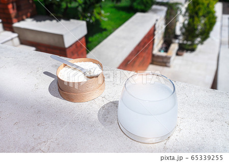 Collagen with a spoon and glass of water on concrete background. Collagen with a spoon and glass of water on concrete background. 65339255