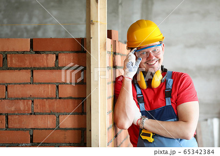 Happy builder stands at brickwork and smiles Happy builder stands at brickwork and smiles 65342384