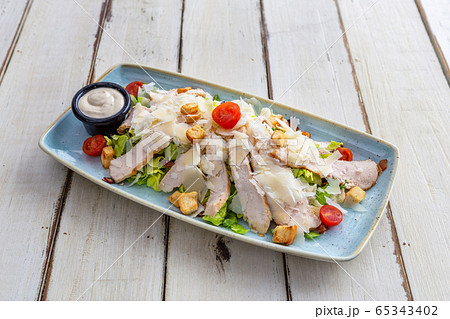 Salad of thinly sliced meat with tomatoes, lettuce and vegetables. White plate on a wooden table. Close-up. Salad of thinly sliced meat with tomatoes, lettuce and vegetables. White plate on a wooden table. Close-up. 65343402