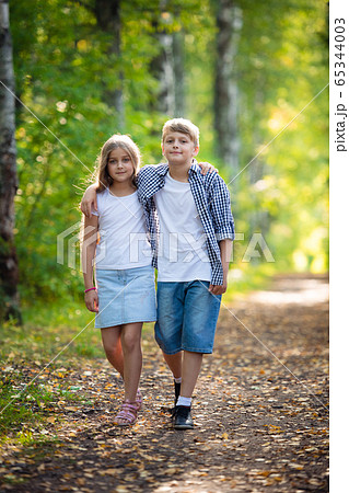 First love. Little boy and girl holding hands and smiling while walking outdoors in park 65344003