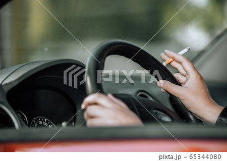 Close up of woman hand smoking cigarette inside the car while driving a vehicle Close up of woman hand smoking cigarette inside the car while driving a vehicle 65344080