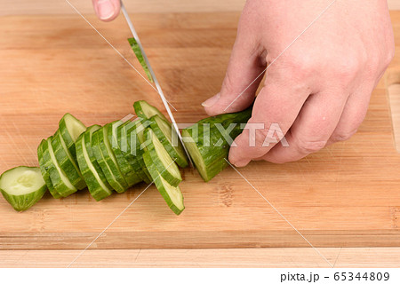 Cutting a cucumber with a knife on a cutting board. 65344809