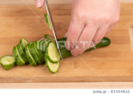 Cutting a cucumber with a knife on a cutting board. 65344810