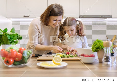 Mother and child cooking together at home in kitchen. Healthy eating, mother teaches daughter to cook Mother and child cooking together at home in kitchen. Healthy eating, mother teaches daughter to cook 65353413