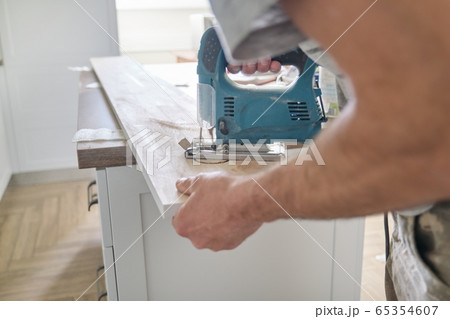 Close-up of carpenters hand using professional woodworking electric tools when working with wood. Male carving hole in wooden panel board, carpentry, woodwork, profession, people 65354607