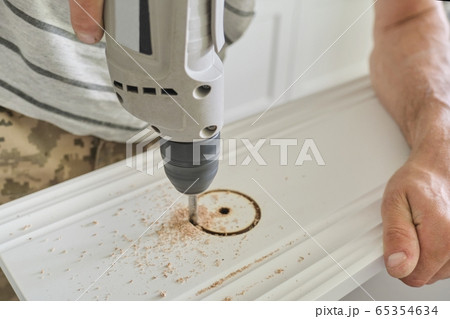 Close-up of carpenters hand using professional woodworking electric tools when working with wood. Male carving hole in wooden panel board, carpentry, woodwork, profession, people Close-up of carpenters hand using professional woodworking electric tools when working with wood. Male carving hole in wooden panel board, carpentry, woodwork, profession, people 65354634