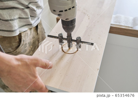 Close-up of carpenters hand using professional woodworking electric tools when working with wood. Male carving hole in wooden panel board, carpentry, woodwork, profession, people 65354676