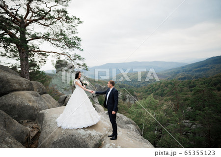 Beautiful gorgeous bride posing to groom and having fun near at mountains with amazing view, space for text, wedding couple Beautiful gorgeous bride posing to groom and having fun near at mountains with amazing view, space for text, wedding couple 65355123