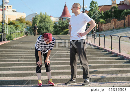 Mature couple in city near the stairs, middle-aged man and woman in sportswear talking resting after running Mature couple in city near the stairs, middle-aged man and woman in sportswear talking resting after running 65356593