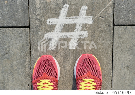 Hashtag symbol on gray sidewalk with woman legs in sneakers, top view Hashtag symbol on gray sidewalk with woman legs in sneakers, top view 65356598