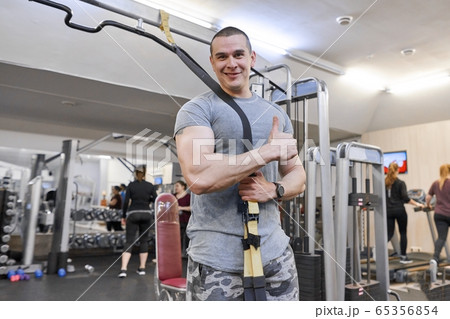 Portrait of young strong smiling muscular smiling man in gym. Male with fitness straps loops 65356854