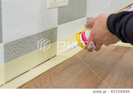 Applying silicone sealant with construction syringe. Worker fills seam between the ceramic tiles on the wall and kitchen worktop 65356900