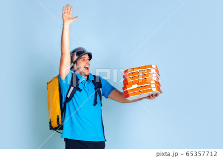 Contacless delivery service during quarantine. Man delivers food and shopping bags during insulation. Emotions of deliveryman isolated on blue background. Contacless delivery service during quarantine. Man delivers food and shopping bags during insulation. Emotions of deliveryman isolated on blue background. 65357712
