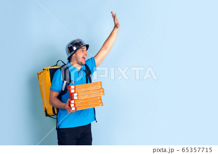 Contacless delivery service during quarantine. Man delivers food and shopping bags during insulation. Emotions of deliveryman isolated on blue background. Contacless delivery service during quarantine. Man delivers food and shopping bags during insulation. Emotions of deliveryman isolated on blue background. 65357715