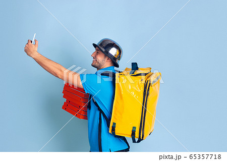 Contacless delivery service during quarantine. Man delivers food and shopping bags during insulation. Emotions of deliveryman isolated on blue background. 65357718
