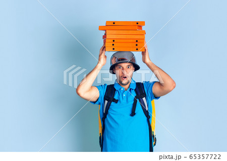Contacless delivery service during quarantine. Man delivers food and shopping bags during insulation. Emotions of deliveryman isolated on blue background. Contacless delivery service during quarantine. Man delivers food and shopping bags during insulation. Emotions of deliveryman isolated on blue background. 65357722
