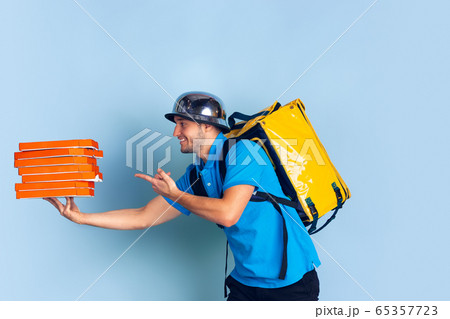 Contacless delivery service during quarantine. Man delivers food and shopping bags during insulation. Emotions of deliveryman isolated on blue background. 65357723
