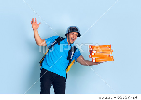 Contacless delivery service during quarantine. Man delivers food and shopping bags during insulation. Emotions of deliveryman isolated on blue background. Contacless delivery service during quarantine. Man delivers food and shopping bags during insulation. Emotions of deliveryman isolated on blue background. 65357724