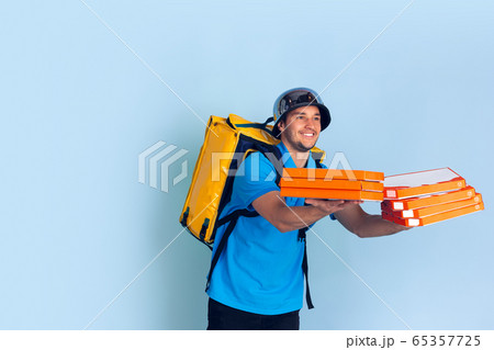 Contacless delivery service during quarantine. Man delivers food and shopping bags during insulation. Emotions of deliveryman isolated on blue background. Contacless delivery service during quarantine. Man delivers food and shopping bags during insulation. Emotions of deliveryman isolated on blue background. 65357725