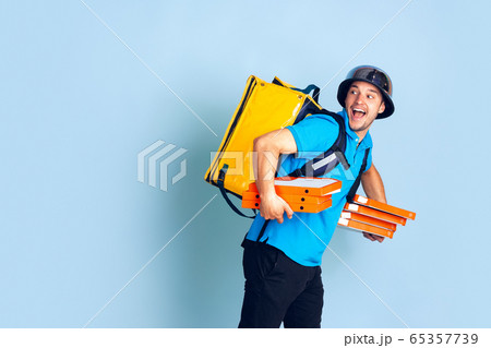 Contacless delivery service during quarantine. Man delivers food and shopping bags during insulation. Emotions of deliveryman isolated on blue background. Contacless delivery service during quarantine. Man delivers food and shopping bags during insulation. Emotions of deliveryman isolated on blue background. 65357739