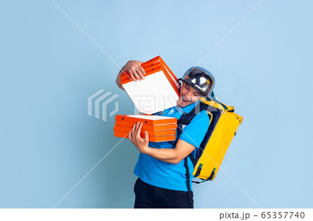 Contacless delivery service during quarantine. Man delivers food and shopping bags during insulation. Emotions of deliveryman isolated on blue background. Contacless delivery service during quarantine. Man delivers food and shopping bags during insulation. Emotions of deliveryman isolated on blue background. 65357740