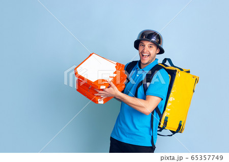 Contacless delivery service during quarantine. Man delivers food and shopping bags during insulation. Emotions of deliveryman isolated on blue background. 65357749