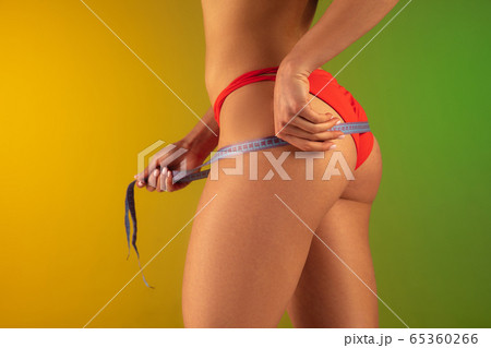 Close up fashion portrait of young fit and sportive woman in stylish red luxury swimwear with measurer on gradient background. Perfect body ready for summertime. Close up fashion portrait of young fit and sportive woman in stylish red luxury swimwear with measurer on gradient background. Perfect body ready for summertime. 65360266