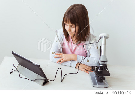 Schoolgirl using microscope in science class. Technologies, lessons and children concept. 65365510