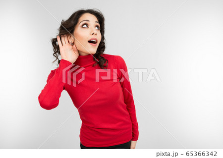 brunette girl in a red sweater overhears a conversation on a white studio background 65366342