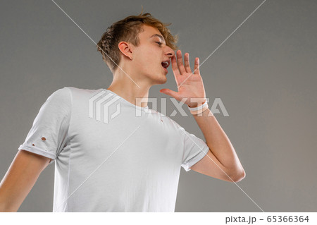 Young caucasian man in white t-shirt posing and gesticulating on camera isolated on grey background 65366364