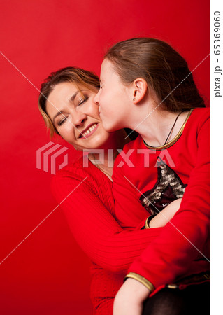 Mom and daughter lovingly cuddle on a red background 65369060