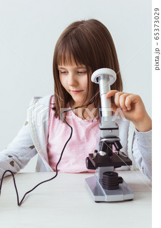 Schoolgirl using microscope in science class. Technologies, lessons and children concept. Schoolgirl using microscope in science class. Technologies, lessons and children concept. 65373029