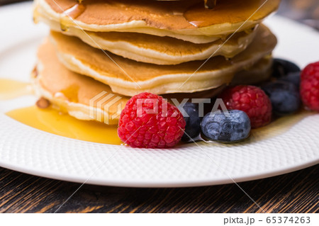 Pile of pancakes with blueberries and raspberries and maple syrup for breakfast on wooden table. Pile of pancakes with blueberries and raspberries and maple syrup for breakfast on wooden table. 65374263