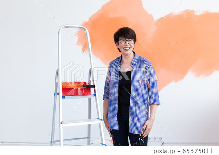 Beautiful middle-aged woman painting wall in her new apartment. Renovation and redecoration concept. Beautiful middle-aged woman painting wall in her new apartment. Renovation and redecoration concept. 65375011