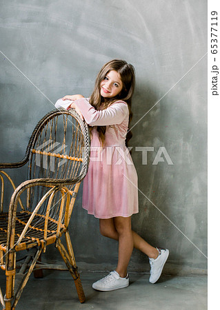 Cute baby girl 5-6 year old wearing stylish pink dress overgrey background. Looking at camera. Birthday party. Celebration. 65377119