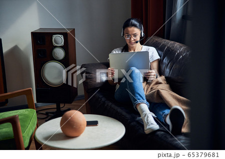 Caucasian serious lady in headphones sitting on sofa with laptop Caucasian serious lady in headphones sitting on sofa with laptop 65379681