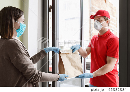 Coronavirus protected deliveryman handing package to client in medical mask and gloves on doorstep of house Coronavirus protected deliveryman handing package to client in medical mask and gloves on doorstep of house 65382384