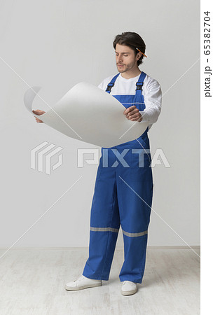 Full-length portrait of young construction engineer checking draft or building plan 65382704