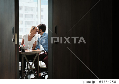 Two Co-Workers Sitting At Office Desk And Kissing Two Co-Workers Sitting At Office Desk And Kissing 65384258